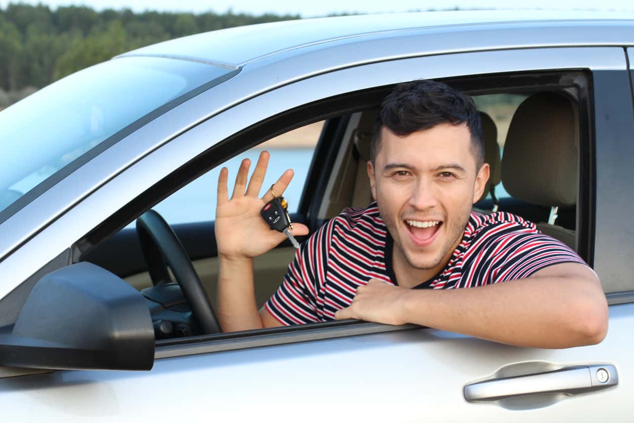 College aged man holding keys inside a car
