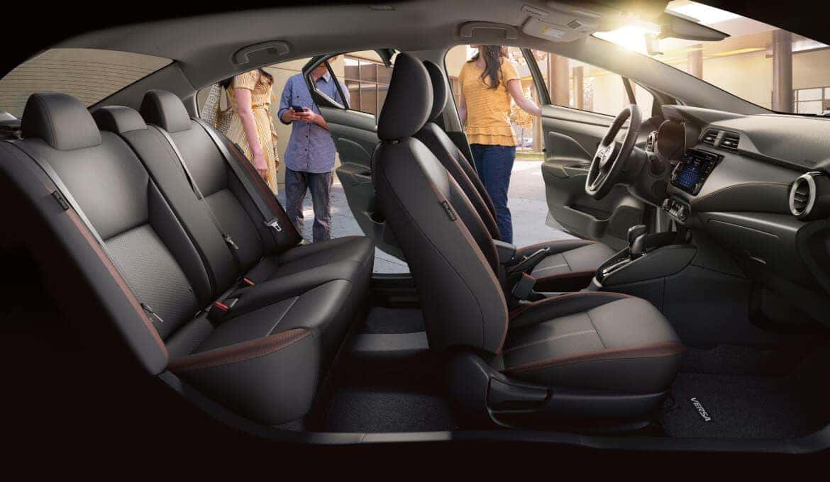 A group of friends outside a Nissan Versa, with its doors open, showcasing the interior.