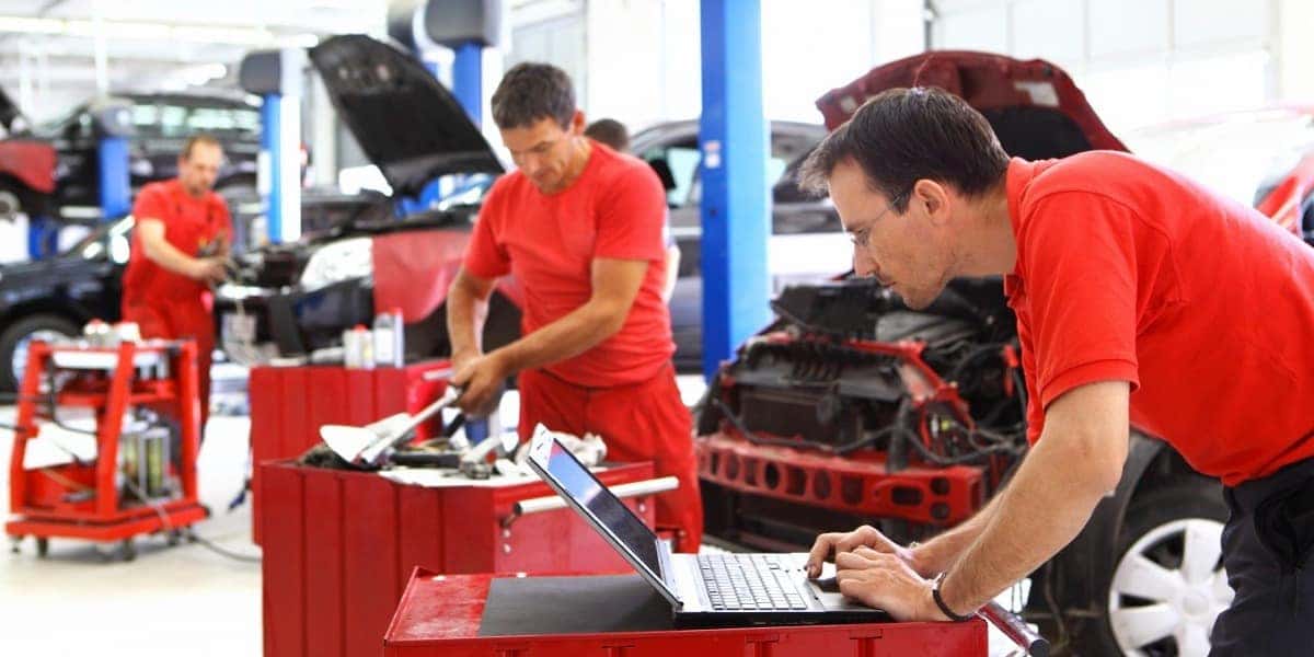 men in red shirts workin on a set of vehicles in the background with tools and an open laptop
