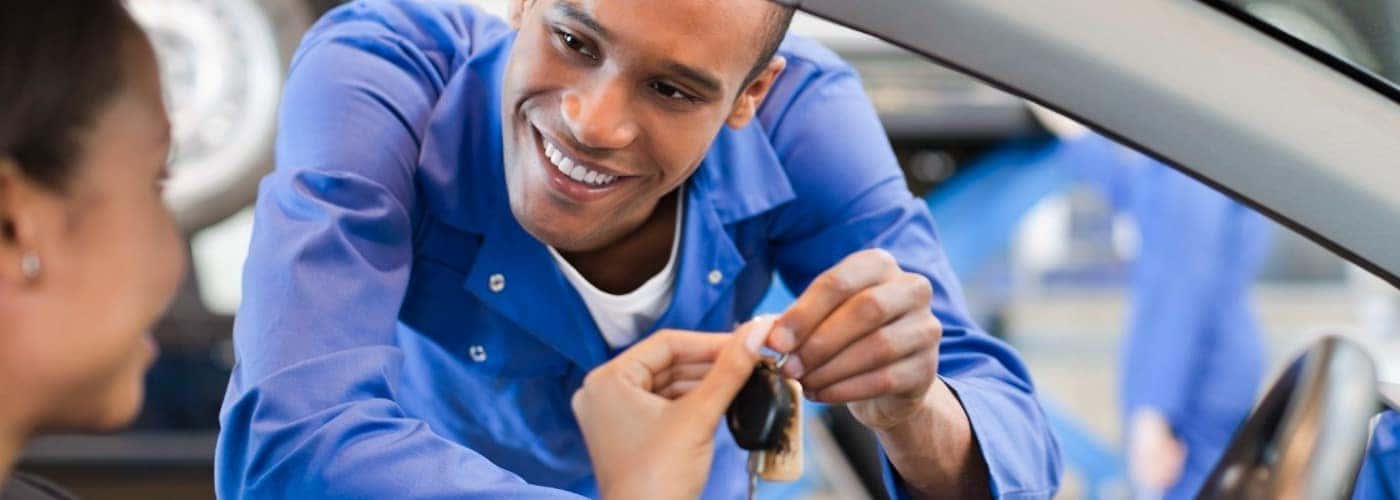 a man in focus handing over a key to an out of focus woman sitting in a car