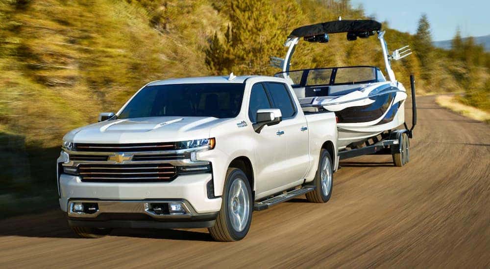 A white 2021 Chevy Silverado 1500 towing a boat on a small country road.