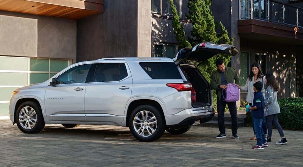 A family loading the trunk of a silver 2021 Chevy Traverse in their driveway.