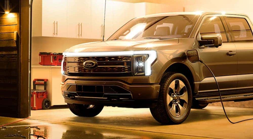 A grey 2022 Ford F-150 Lightning charging in a residential garage at night.
