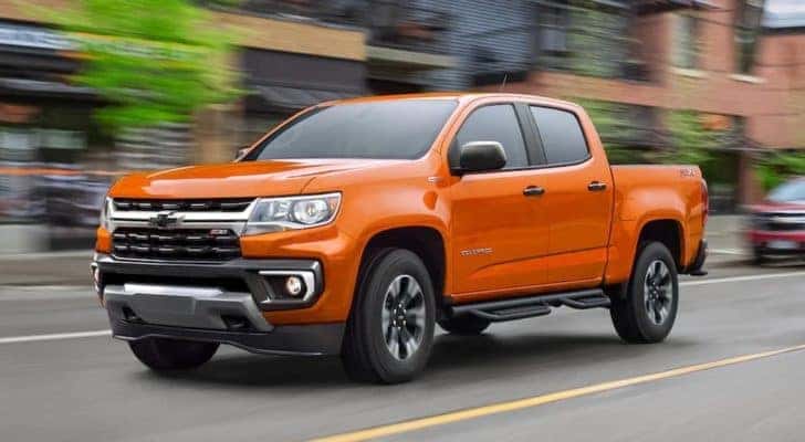 An orange 2021 Chevy Colorado Z71 is driving down a city street.