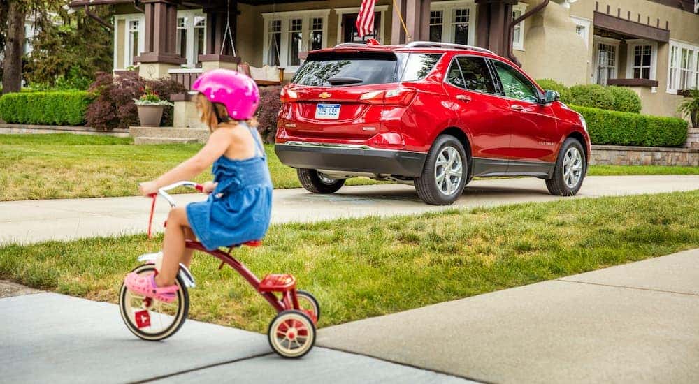 A kid riding a tricycle past a red 2021 Chevy Equinox in a suburban driveway.