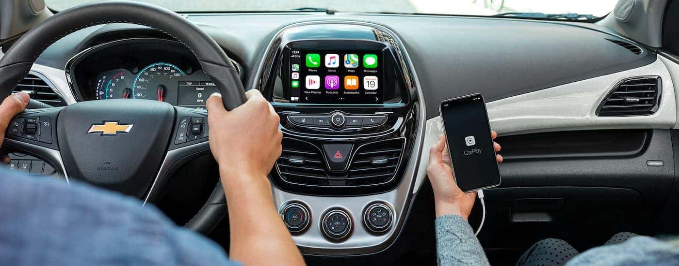 The infotainment screen and a smart phone are shown being used in a 2020 Chevy Spark.