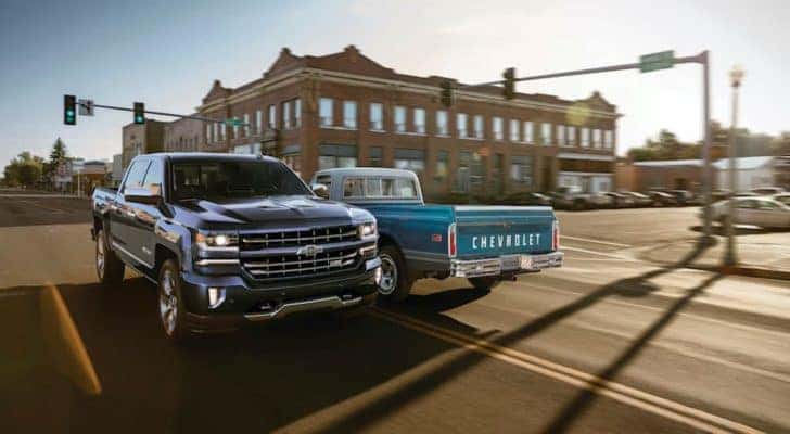 A dark blue 2018 Chevy Silverado 1500 Z71 Centennial Edition is passing a light blue 1972 C10 next to a set of traffic lights.