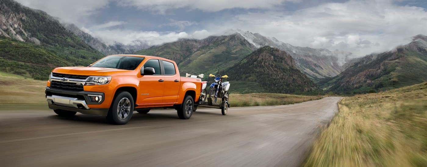 An orange 2021 Chevy Colorado is shown towing dirt bikes past distant mountains.