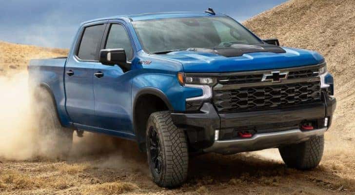 A blue 2022 Chevy Silverado 1500 is shown from the front off-roading in a sand pit.