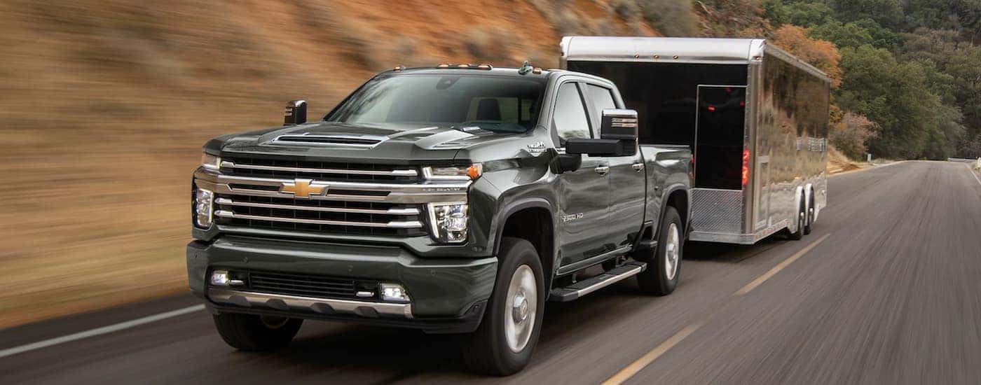 A green 2022 Chevy Silverado 2500 is shown towing a trailer on an open road after leaving a Chevy Silverado dealership.