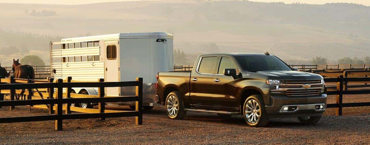 A black 2022 Chevy Silverado 1500 High Country is shown towing a horse trailer.