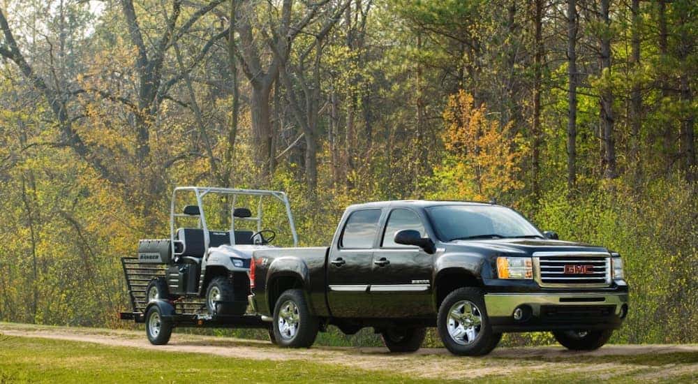 A black 2014 GMC Sierra 1500 towing a golf cart on a trailer.