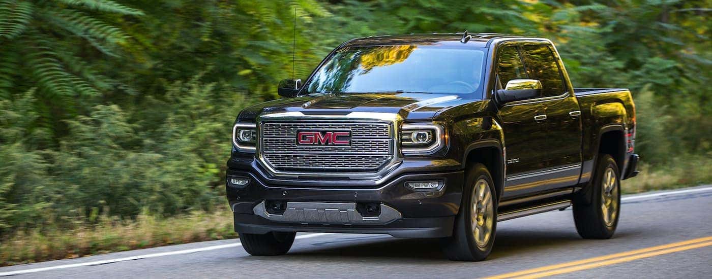 A black 2016 GMC Sierra 1500 Denali is shown driving on a tree-lined road.