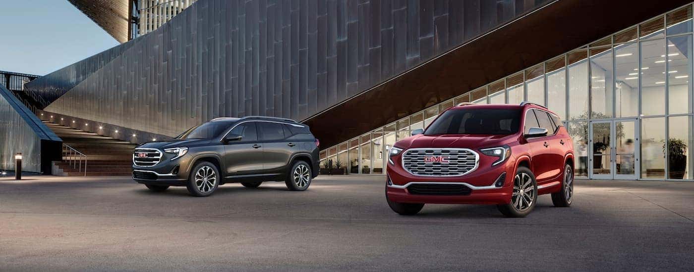 A grey 2018 GMC Terrain SLT and a red Terrain Denali are shown in front of a modern building.