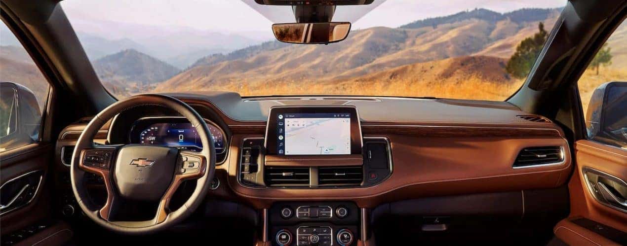 The black and brown interior of a 2022 Chevy Suburban shows the steering wheel and infotainment screen.