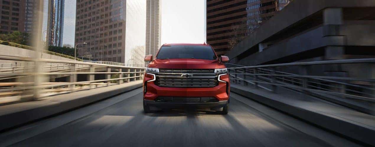 A red 2022 Chevy Tahoe is shown from the front driving on a city street.