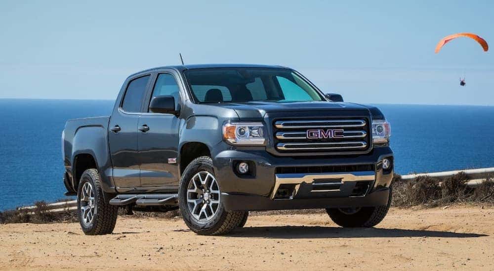 A popular used GMC truck, a black 2018 Canyon All Terrain parked on a beach with parasailers nearby.