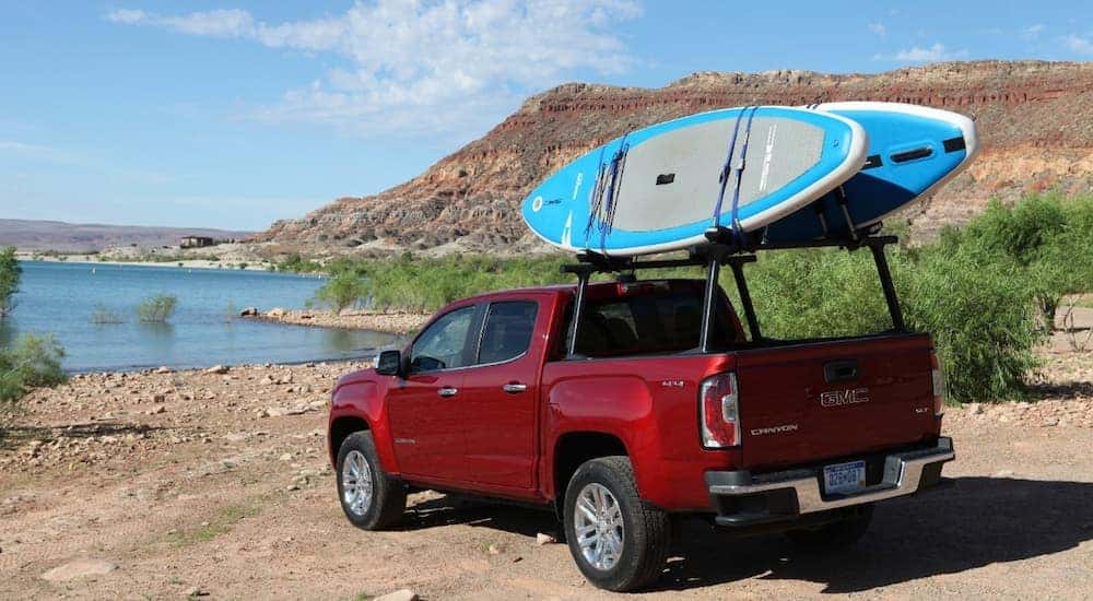 A red 2019 GMC Canyon with paddle boards attached to a rack, parked at a lake.