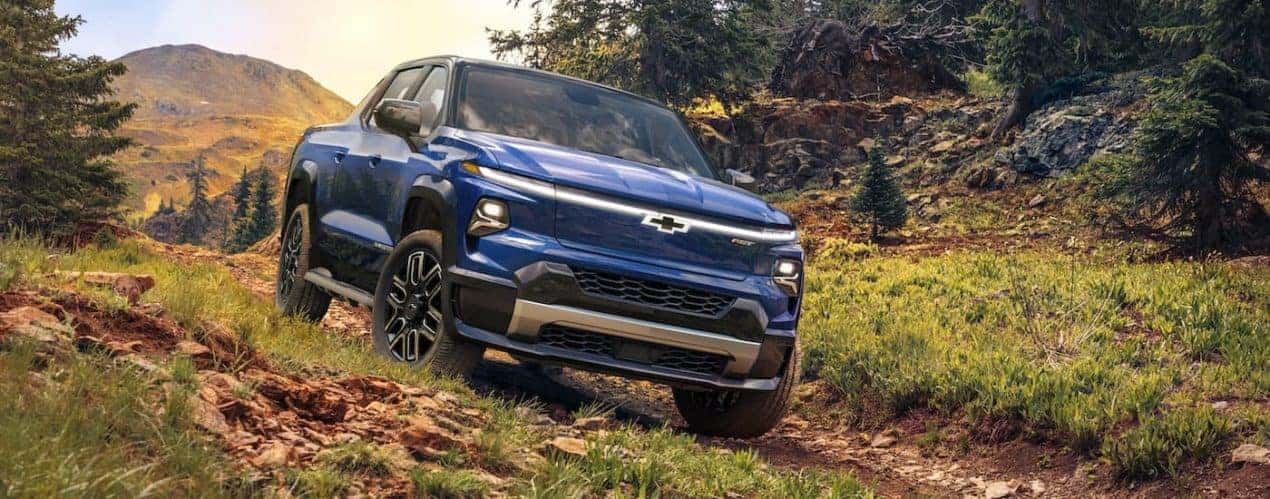 A blue 2024 Chevy Silverado EV RST is shown driving on a trail.