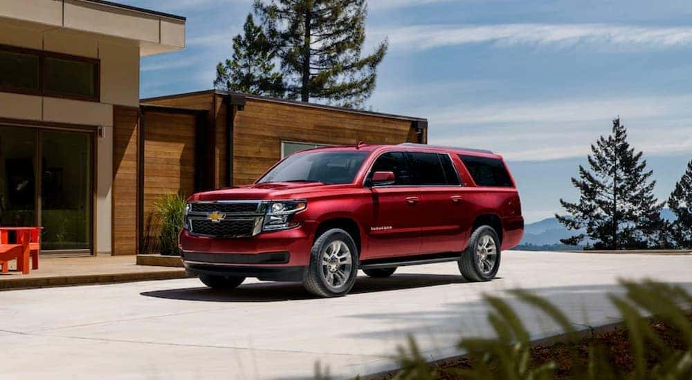A red 2020 Chevy Suburban parked in front of a modern house overlooking mountains.