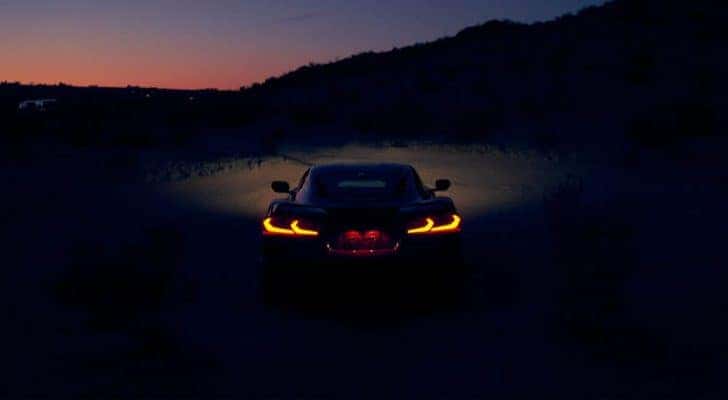 A red 2021 Chevy Corvette is shown from the rear with its lights illuminated at dusk.