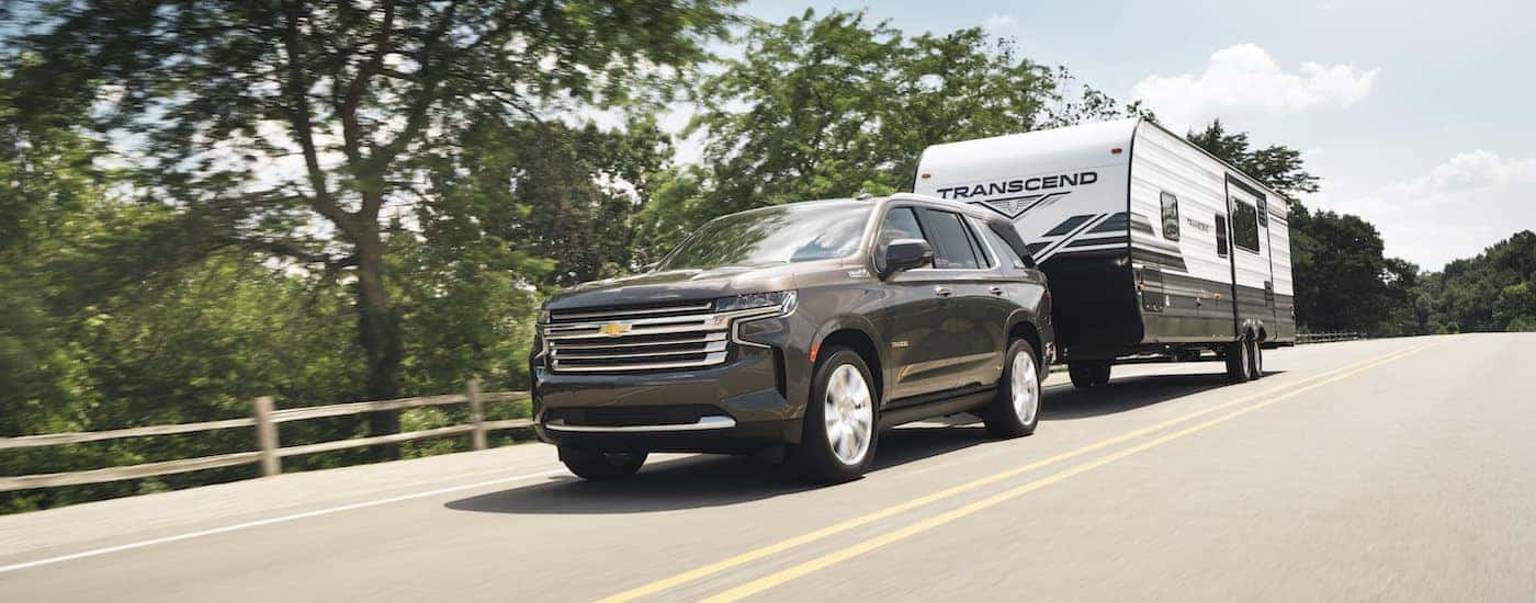 A grey 2021 Chevy Tahoe High Country is shown towing a trailer on a tree-lined road.
