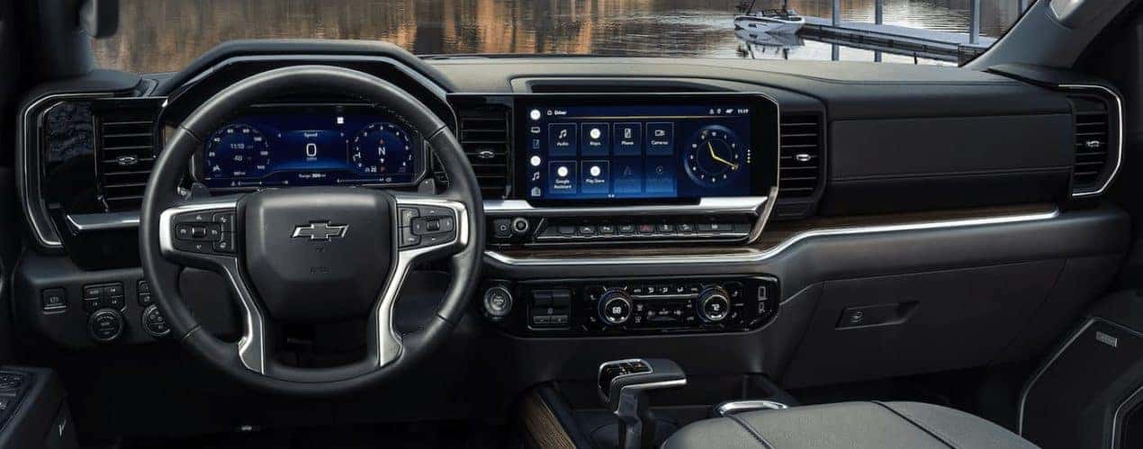 The black and grey interior of a 2023 Chevy Silverado 1500 shows the steering wheel and infotainment screen.