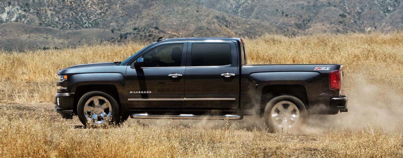 A black 2018 Chevy Silverado Z71 is shown from the side parked in a dry grassy field.