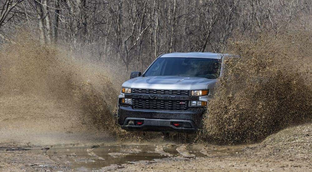 A silver 2020 Chevy Silverado 1500 Trail Boss splashes mud and water as it drives through a puddle