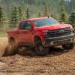 A red 2020 Chevy Silverado 1500 kicks up dust in a dirt pit while off-roading