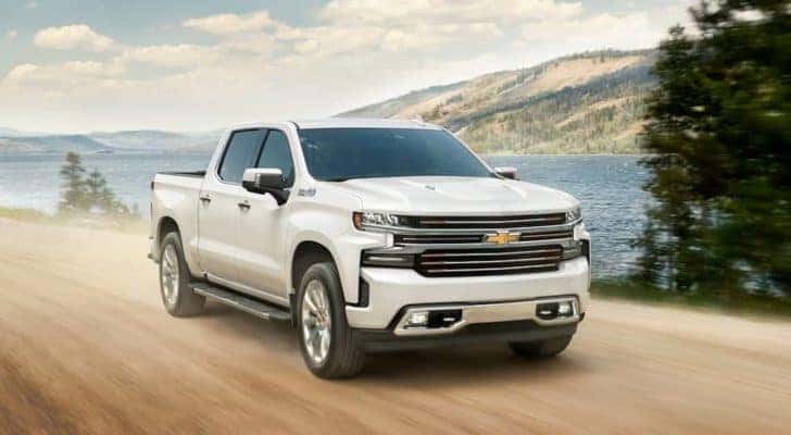 A white 2020 Chevy Silverado 1500 High Country is shown driving past a lake and mountains.
