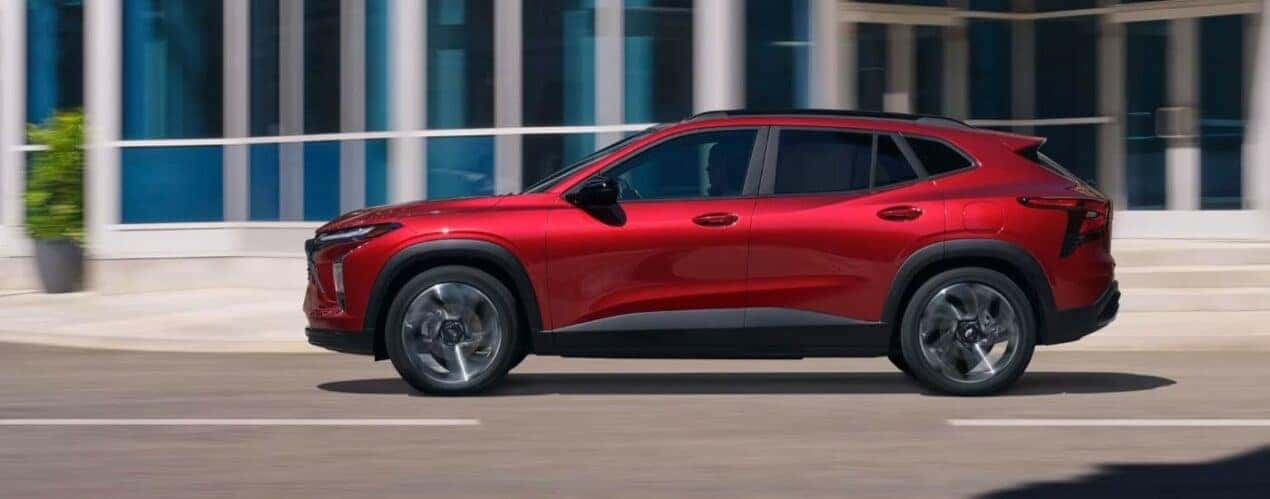 A red 2024 Chevy Trax RS is shown from the side driving on a city street.
