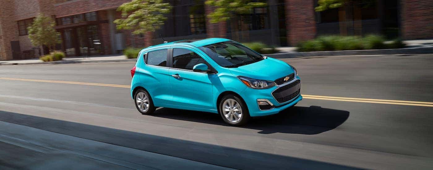 A teal 2021 Chevy Spark is shown driving on a city street.