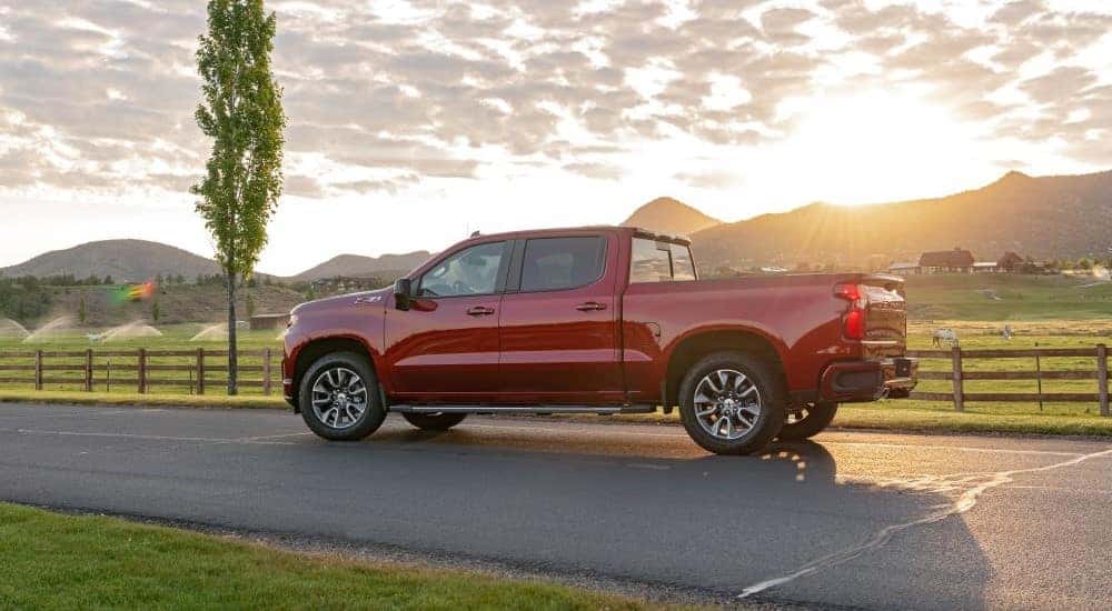 A red 2020 Chevy Silverado 1500 Z71 driving past a horse paddock on a sunny day.