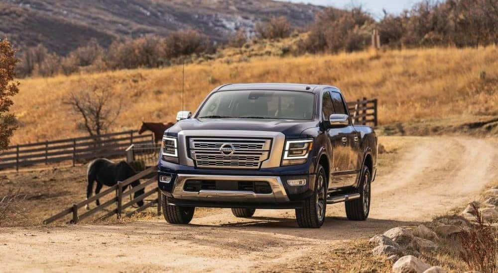 A dark blue 2021 Nissan Titan driving past horses on a farm road