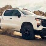 A white 2024 Chevy Silverado 1500 Z71 Custom Trail Boss kicks up dust while off-roading in the desert