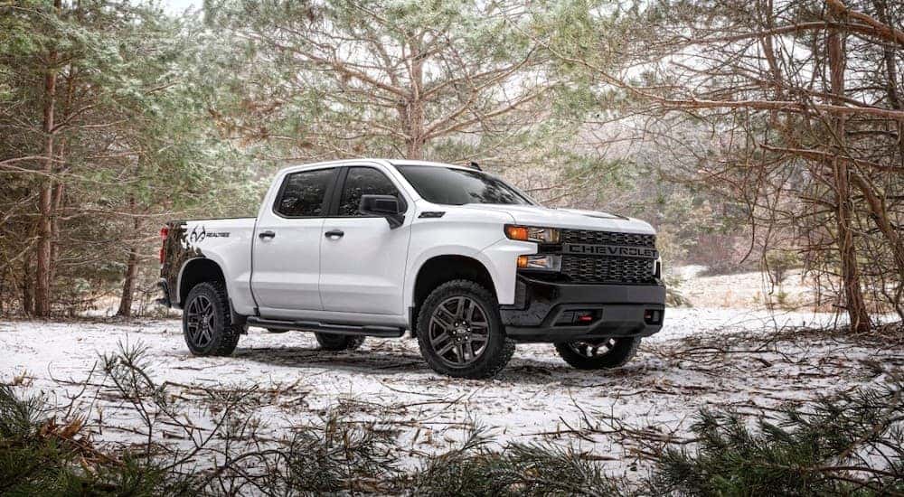 A white 2021 Chevy Silverado 1500 Realtree Edition is shown parked off-road in a forest.