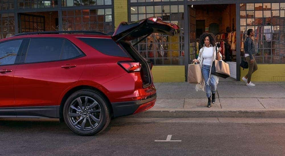 A person is shown carrying bags near a red 2024 Chevy Equinox RS.
