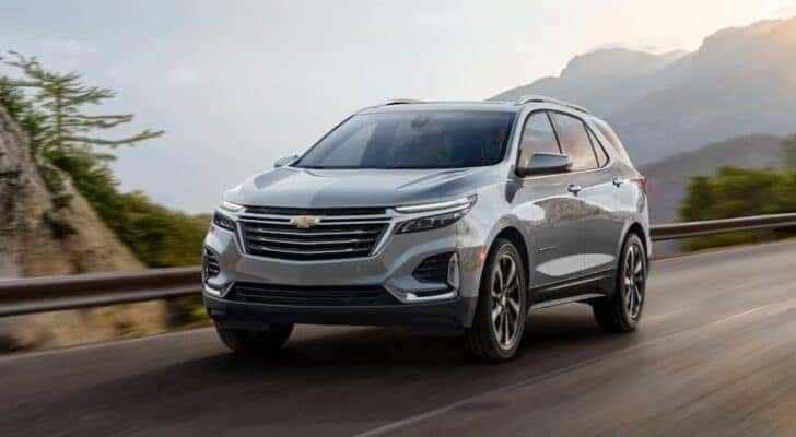 A popular Chevy Equinox for sale near me, a silver 2024 Chevy Equinox, is shown driving on a highway.