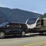 A black 2024 Chevy Suburban High Country towing a large camper on a mountain road.
