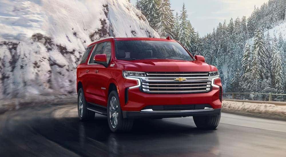 A red 2024 Chevy Suburban High Country driving on a snowy road.