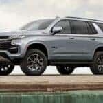 A grey 2024 Chevy Tahoe Z71 is shown parked near a dealership with Chevy SUVs for sale.