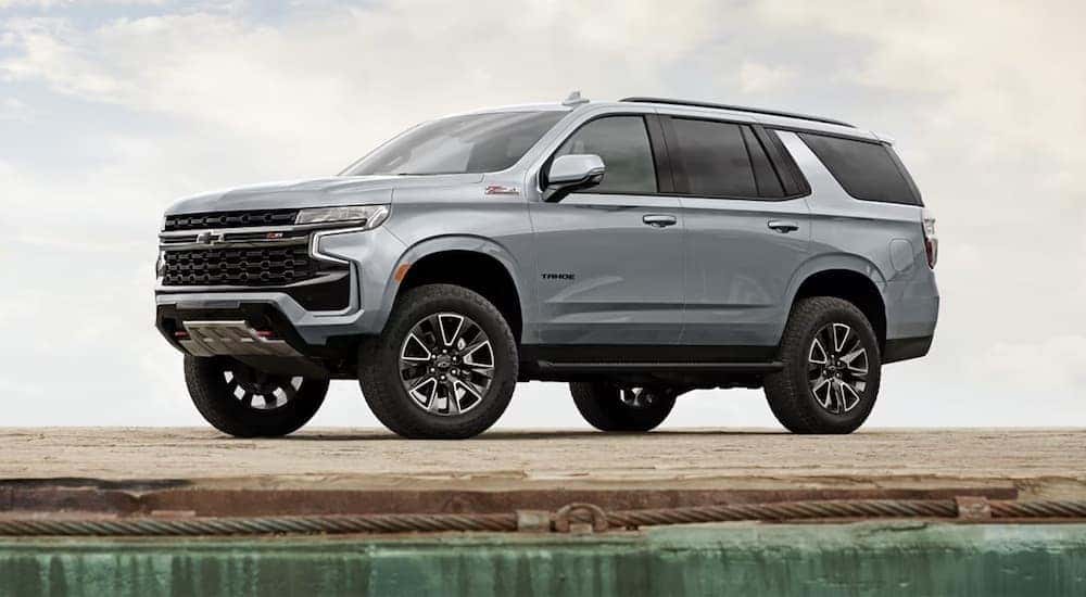 A grey 2024 Chevy Tahoe Z71 is shown parked near a dealership with Chevy SUVs for sale.