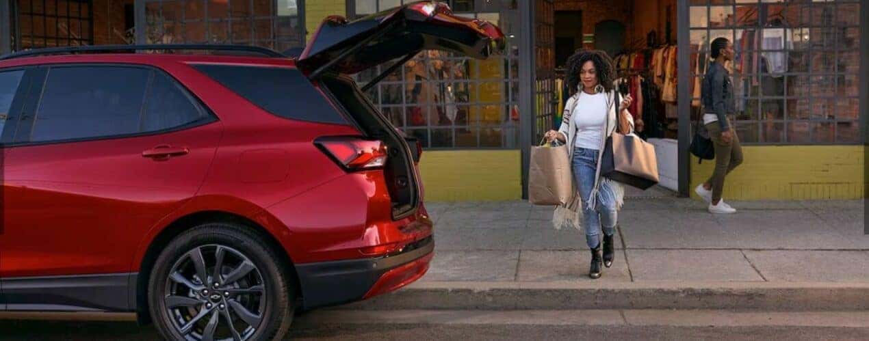A person is shown carrying shopping bags towards the open hatchback of a red 2024 Chevy Equinox RS after a 2024 Chevy Equinox vs 2024 Mitsubishi Eclipse Cross comparison.