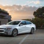 White 2016 Chevy Malibu parked next to a cement building and trees