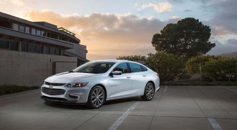 White 2016 Chevy Malibu parked next to a cement building and trees