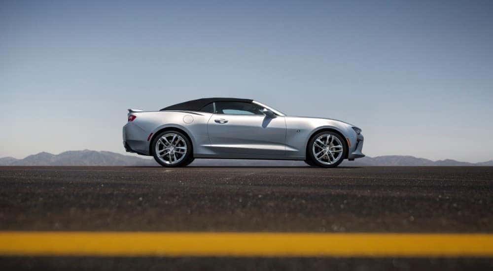 Side view of a silver 2016 Camaro Convertible driving on a road in front of mountains