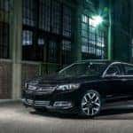 Black 2016 Chevrolet Impala Midnight Edition parked in a dark alley next to a brick building with large windows