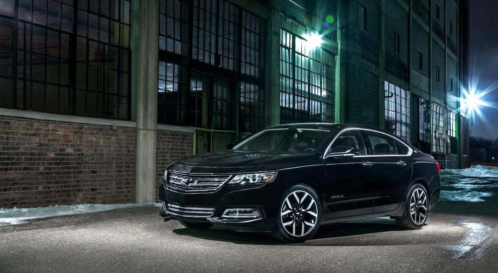 Black 2016 Chevrolet Impala Midnight Edition parked in a dark alley next to a brick building with large windows
