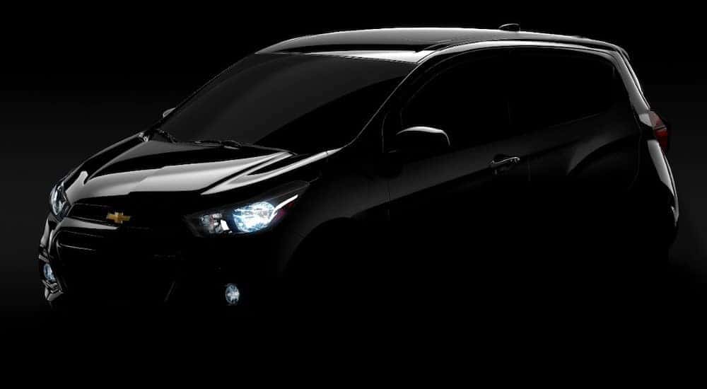 Black 2016 Chevrolet Spark parked in an all black, dark room with its headlights on